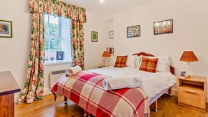 Ein Schlafzimmer mit einem Bett, zwei Nachttischen, einem fenster mit Vorhängen, einer Chandelier und Wandbildern.