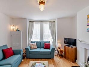 Ein Wohnzimmer mit einer Couch, einem Fernseher, einer Lampe und einem Kamin.