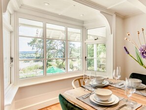 A dining area with a table set for four, large windows with a view of greenery and hills, and a vase with flowers on the table. - 4 Bed in Pulborough (oc-89346) (Fittleworth)