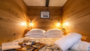 Ein gemütlicher Holzraum mit einem Bett, zwei Wandlampen, einem gerahmten Bild und einer Ablage mit Speisen und Getränken.