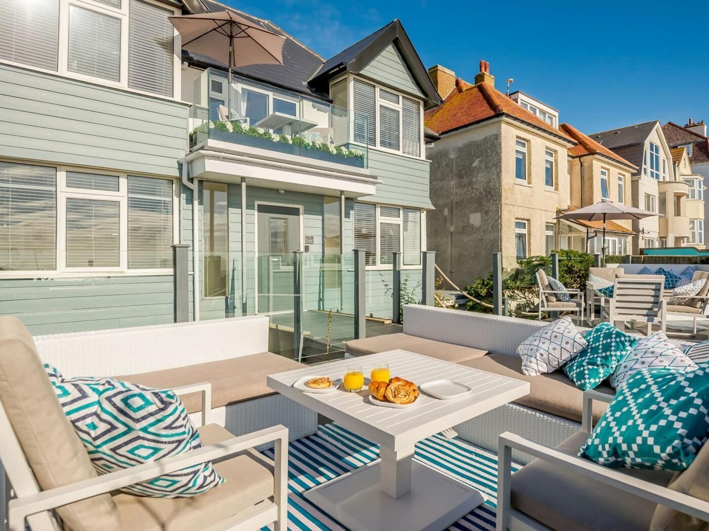Een terras met buitenplaatsen, een tafel met ontbijtartikelen en een uitzicht op omliggende huizen.