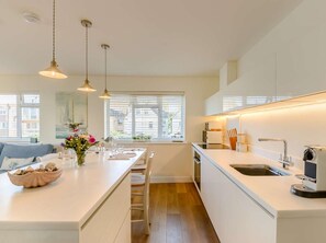 Une cuisine moderne dotée d’un îlot central, de meubles blancs et d’un éclairage suspendu.