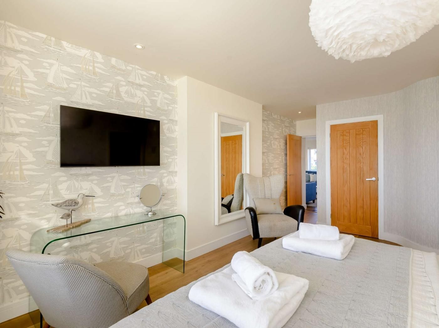 Een hotelkamer met een bed, een glazen tafel, een stoel, een televisie en een spiegel.