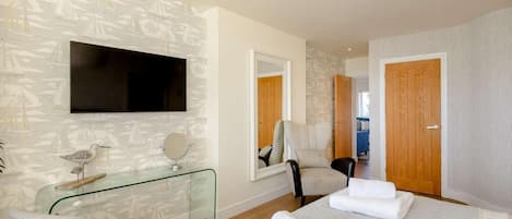 A hotel room with a bed, a glass table, a chair, a TV, and a mirror.