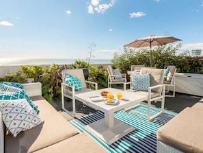An outdoor seating area with lounge chairs and a table, a view of the sea, and a 'For Sale' sign. - 1 Bed in Hythe (oc-89968) (Hythe)