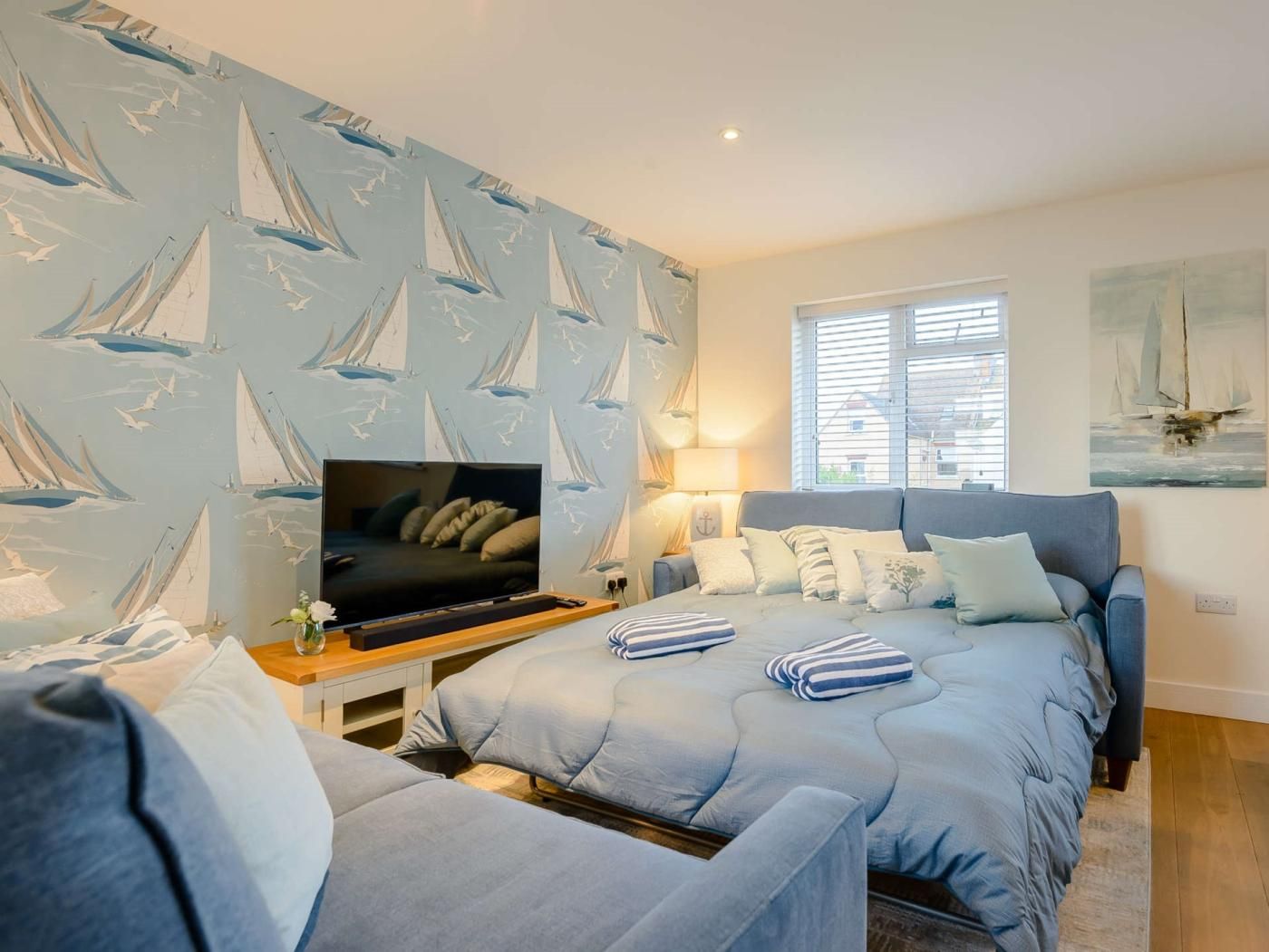 A bedroom with a bed, a TV, a sofa, and a window with blinds.