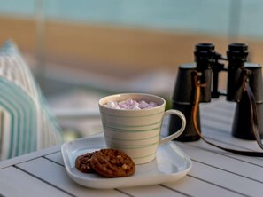 A cup of hot chocolate with marshmallows on a white saucer, a cookie, binoculars, and a striped pillow on a white table. - 1 Bed in Hythe (oc-89970) (Hythe)