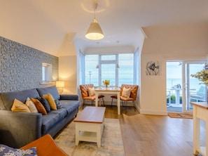 A living room with a sofa, chairs, a coffee table, and a dining table. There is a window with blinds, a hanging light fixture, and a view of the sea through the glass door. - 1 Bed in Hythe (oc-89970) (Hythe)