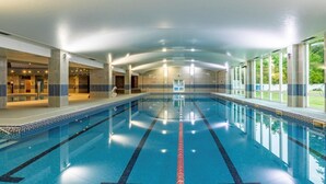 Una piscina interna con corsie ben delimitate, pavimento piastrellato e vista sull'esterno attraverso ampie finestre.