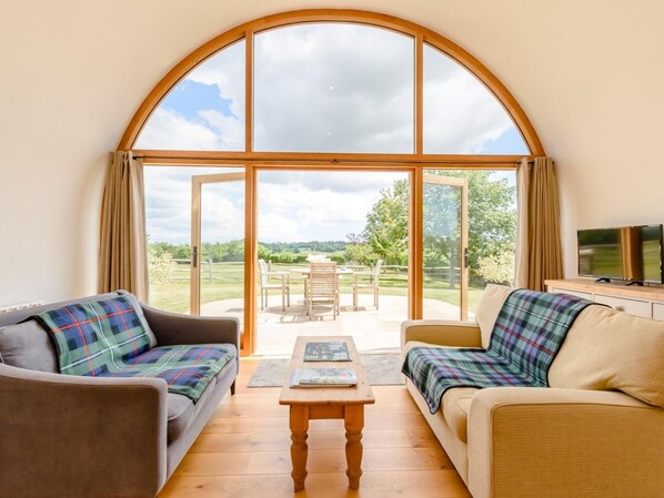 A room with a large arched window, a sofa, a coffee table, and a television.