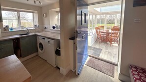 A compact kitchen with a washing machine, a dining area with chairs, and a large glass door leading to a patio. - 2 Bed in Brecon (oc-51153) (Llandefalle)