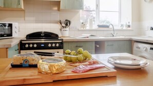 A kitchen with a stove, microwave, and a cutting board with cheese and fruit. - 2 Bed in Brecon (oc-51153) (Llandefalle)