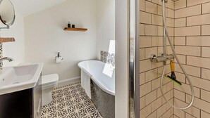Un baño con lavamanos, inodoro y bañera blancos, ducha con puerta de cristal y un tragaluz sobre el inodoro.