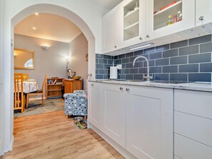 A kitchen with white cabinets, a blue tiled backsplash, and a wooden dining table with chairs. - 3 Bed in Great Yarmouth (oc-93210) (Winterton-on-Sea)