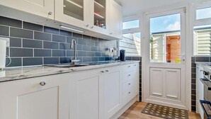 Una cucina moderna con mobili bianchi, una parete di fondo rivestita di piastrelle grigie e una finestra con vista all'esterno.