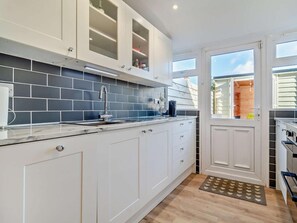 A modern kitchen with white cabinets, a grey tiled backsplash, and a window with a view of the outside. - 3 Bed in Great Yarmouth (oc-93210) (Winterton-on-Sea)