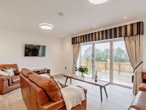 A living room with a sofa, a coffee table, a TV mounted on the wall, and a sliding glass door leading to an outdoor area.