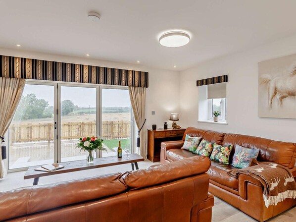 A spacious living room with a leather sofa, a wooden coffee table, and a large window with curtains.