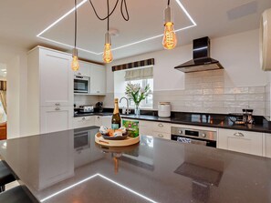Een moderne keuken met een groot eiland, witte kastjes, een inbouwoven en hanglampen.