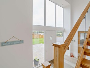 Een modern interieur met een houten trap, een glazen deur naar een terras en een bord met daarop 'BEACH HOUSE'.