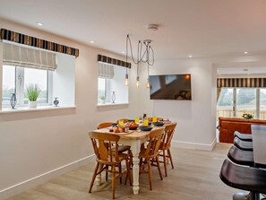 A dining area with a round table, wooden chairs, and a TV mounted on the wall.