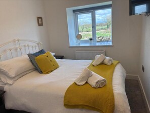 Een net opgemaakt bed met kussens en dekens, een raam met uitzicht op de omgeving, en een bordje met de tekst 'Slaap' aan de muur.