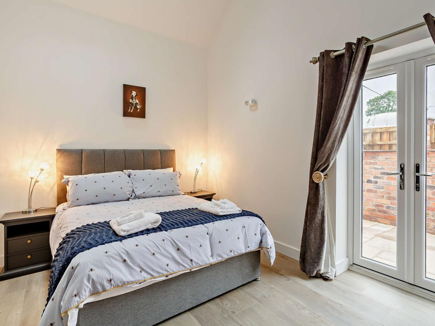 Un dormitorio con cama, mesitas de noche, una obra de arte en la pared y vistas a través de una puerta de cristal.