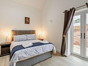 Een slaapkamer met een bed, nachtkastjes, een kunstwerk aan de muur en uitzicht door een glazen deur.