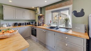 Una cocina moderna con armarios grises, encimera de madera, horno empotrado, lavamanos y ventana con vistas al exterior.