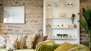 Sala de estar con un sofá verde, un estante blanco con adornos, un dibujo enmarcado en la pared y una planta grande.