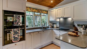 Una cucina moderna con mobili bianchi, soffitto in legno e una finestra che si affaccia sul verde.