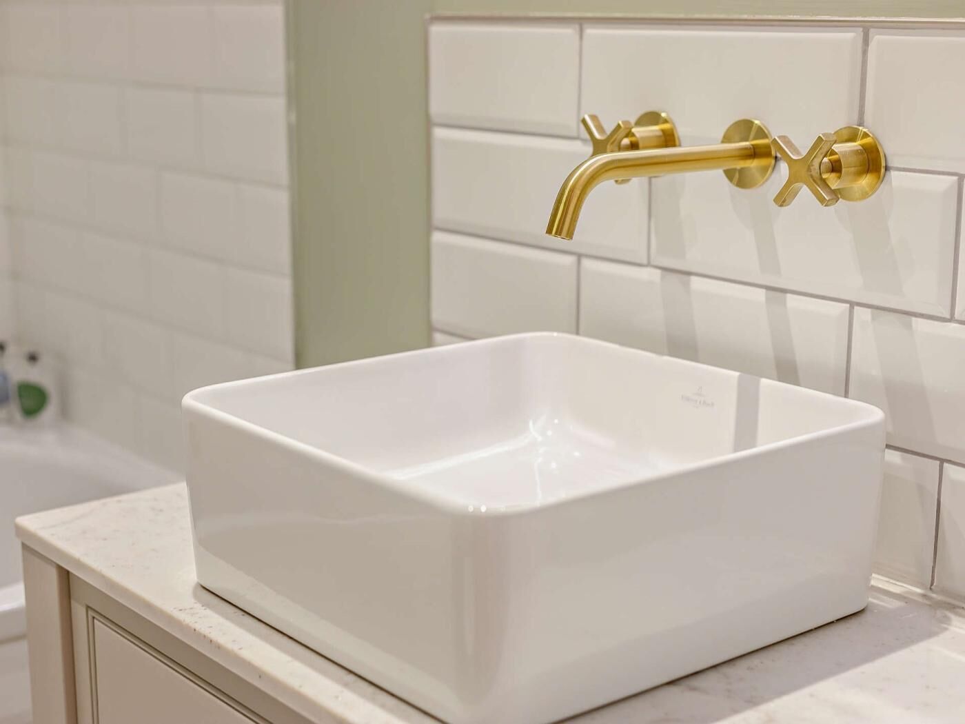 Ein weißes, rechteckiges Waschtuch mit goldenem Wasserhahn, an einer weißen, gefliesten Wand befestigt.