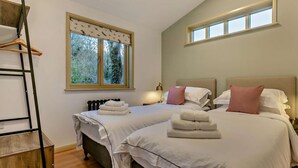 Una camera da letto con due letti, pavimento in legno, finestra vista alberi e lampadario.