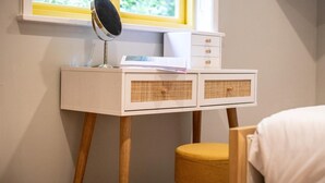 Et hvidt skrivebord med en lampe, et spejl og en lille kommode op ad en væg med et vindue.