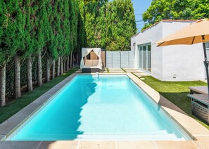 Ein rechteckiger Pool mit einer Fliesenbordsteinkante, umgeben von einem gepflegten Rasen und einer Baumreihe.