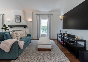 Ein modernes Wohnzimmer mit einem türkisfarbenen Sofa, einem weißen Hocker, einem Flachbildfernseher und einer schwarzen Unterhaltungsanlage.