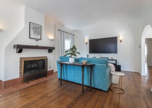 Ein Wohnzimmer mit Kamin, einem blauen Sofa, einem Couchtisch und einem an der Wand befestigten Flachbildfernseher.
