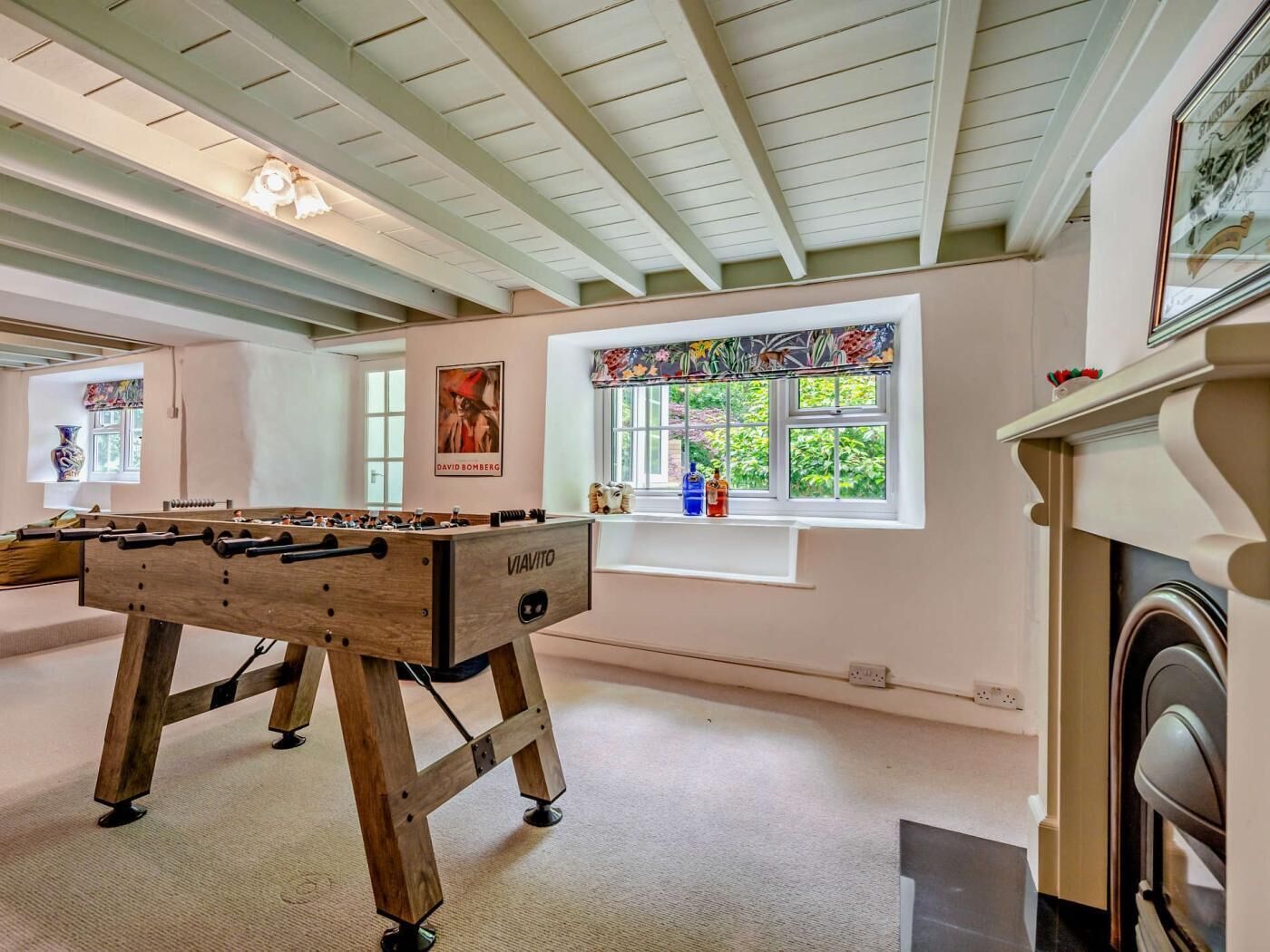 A room with a foosball table, a window with a view of greenery, and a fireplace.