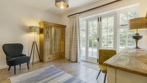 A room with a wooden cabinet, a desk, a chair, a floor lamp, and a large window with curtains. - 3 Bed in Hereford (oc-93304) (Bodenham)