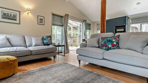 A modern living room with two grey sofas, a wooden floor, and a large window. - 2 Bed in Truro (oc-93310) (Porthtowan)