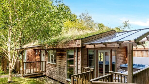 A wooden cabin with a deck, large windows, and a hot tub. - 2 Bed in Truro (oc-93310) (Porthtowan)