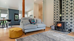 A modern living room with a sofa, ottoman, and a fireplace. - 2 Bed in Truro (oc-93310) (Porthtowan)