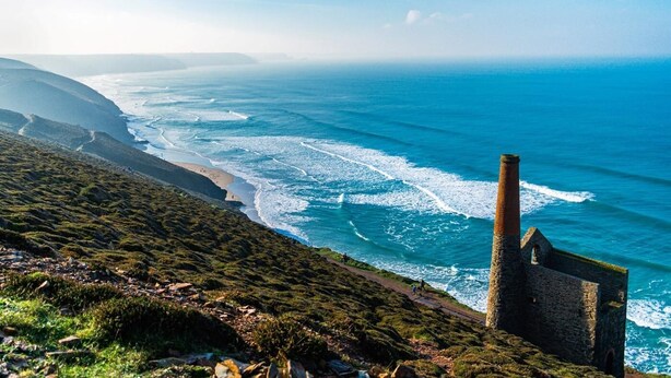 A coastal landscape with a stone structure, a beach, and ocean waves.