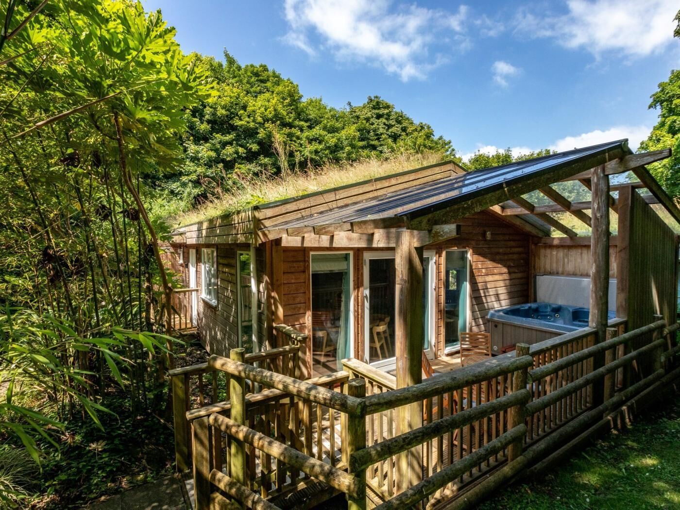 En træhytte med jacuzzi, omgivet af en træterrasse og frodig vegetation.