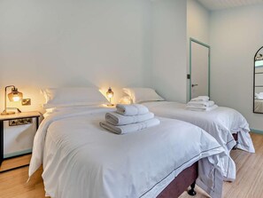 A hotel room with two beds, each with neatly folded white towels, bedside lamps, and a mirror on the wall. - 3 Bed in Truro (oc-93312) (Porthtowan)