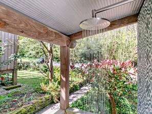 A wooden pergola with a showerhead, surrounded by a garden with various plants and a patterned wall. - 3 Bed in Truro (oc-93312) (Porthtowan)