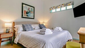 A neatly made bed with pillows, a bedside lamp, a framed abstract painting, and a small table with a lamp.