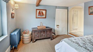 Ein Schlafzimmer mit einem Bett, einer Holzkiste, einem Korbwägelchen, einer Heizung und einer Tür.