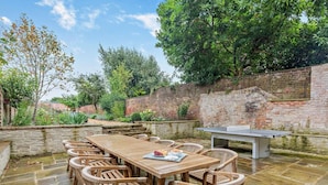 Eine Terrasse im Freien mit einem Tischtennisschläger, Holzstühlen und einem Steinfußboden.