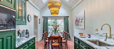 Een keuken met groene kastjes, een eettafel met stoelen, een hanglamp en een raam met gordijnen.